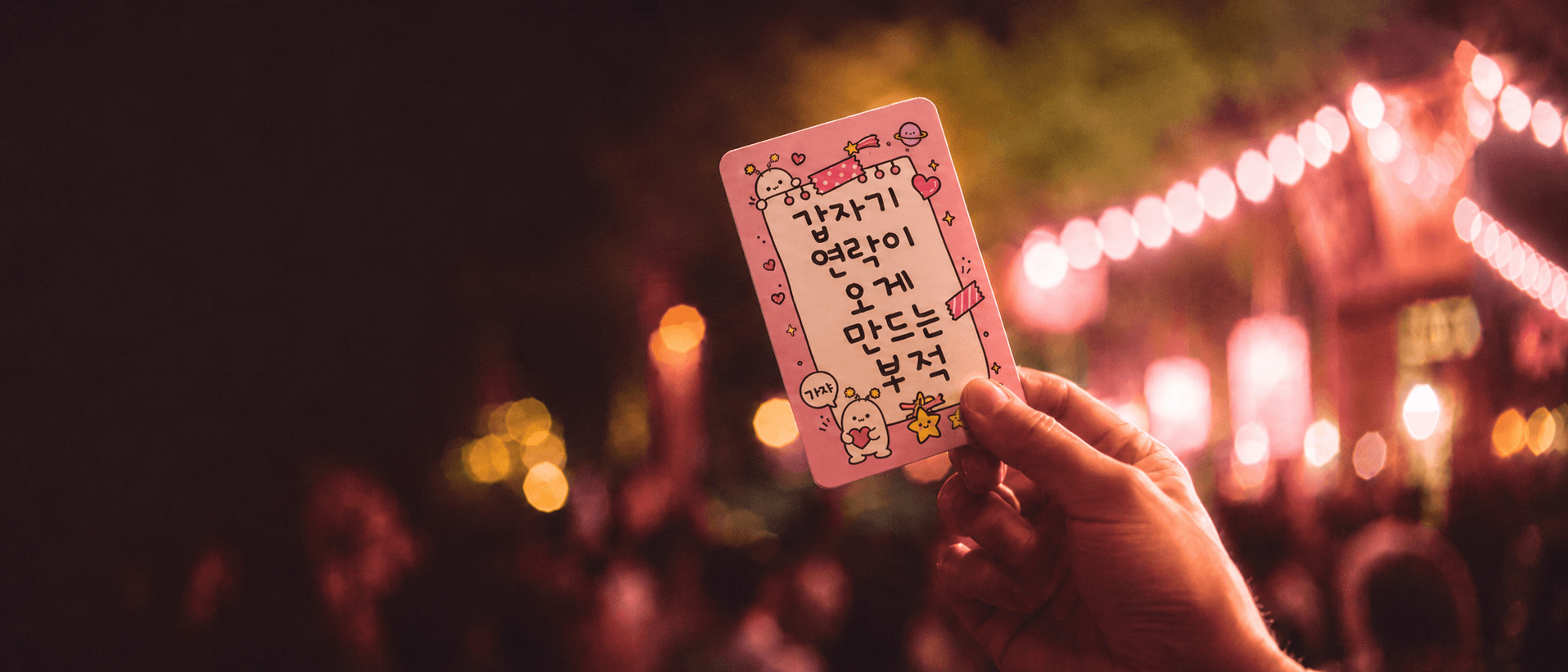 야간 축제 현장에서 부적 카드를 들고 있는 손